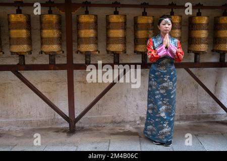 Ein chinesischer Tourist posiert für ein Foto in traditioneller tibetischer Kleidung vor Gebetsrädern. Lhasa. Autonome Region Tibet. China. Stockfoto