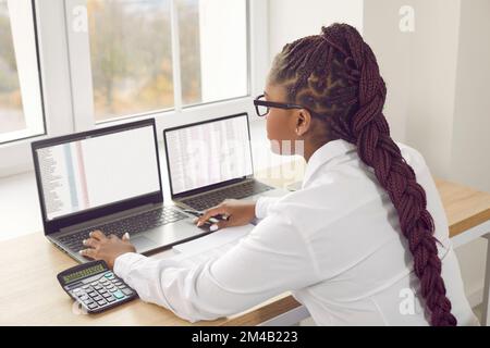 Afroamerikanische Buchhalterin, die im Büro arbeitet, an ihrem Schreibtisch sitzt und Laptops verwendet Stockfoto