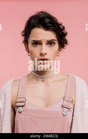 Eine besorgte Frau in Gürtelkleid und Perlenkette, die auf Pink isoliert auf die Kamera schaut Stockfoto