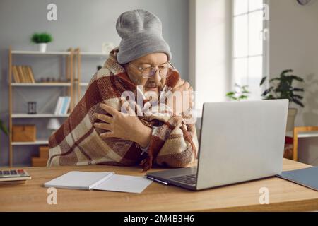 Älterer Mann mit Hut, der am Computer sitzt und in Karo verpackt ist Stockfoto