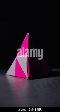 Eine vertikale Aufnahme einer pinkfarbenen und weißen Origami-Pyramide auf einer schwarzen Oberfläche Stockfoto