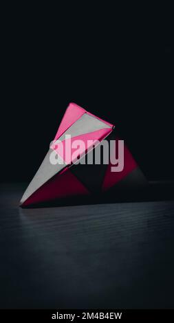 Eine vertikale Aufnahme einer pinkfarbenen und weißen Origami-Pyramide auf einer schwarzen Oberfläche Stockfoto
