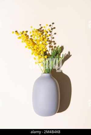 Ein Strauß gelber Mimosablüten steht in einer Keramikvase mit Schatten auf gelbem Hintergrund. Konzept vom 8. März, fröhlicher Frauentag. Draufsicht und Stockfoto