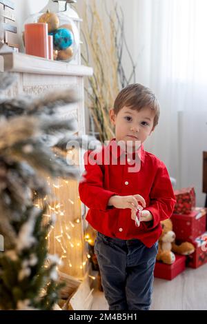 Fröhliches, süßes Kind an Weihnachten, Urlaub genießen, Geschenke öffnen und Kekse essen Stockfoto