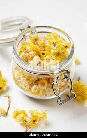 Helichrysum italicum. Gelb getrocknete Kräuterblumen in einem Glas Nahaufnahme auf weißem Hintergrund. Stockfoto