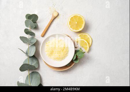 Gelbes Meersalz aus biologischem Anbau mit Zitrone und Eukalyptuszweig auf weißem, strukturiertem Hintergrund. Das Konzept von Spa und Wellness. Draufsicht und Kopierbereich. Stockfoto