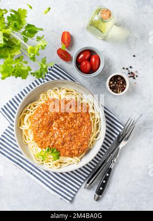 Köstliche Pasta Bolognese mit Tomatensauce, Parmesankäse und frischen Kräutern auf einem Teller auf hellem Hintergrund mit Tomaten und Olivenöl. Das Konzept Stockfoto