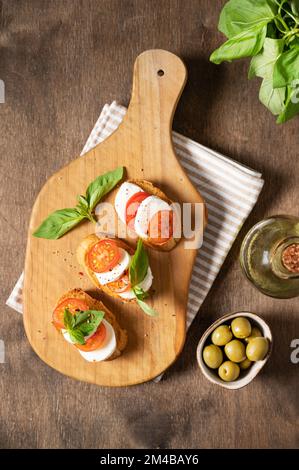 Caprese-Sandwiches mit frischen Tomaten, Mozzarella-Käse und frischem Basilikum und Toast auf einem Schneidebrett mit Gewürzen und Olivenöl auf einem hölzernen Backgrou Stockfoto