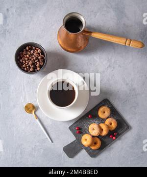 Köstliches Frühstück mit frisch gebrühtem Kaffee und Mini-Donuts in Puderzucker und Preiselbeeren auf schwarzem Schiefer auf blauem Hintergrund. Oben vi Stockfoto