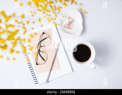 Flach liegend mit gelber Mimosablüte, einer Tasse Kaffee, einer Brille, einem handgefertigten Notizbuch auf einem Marmortisch. Geblümter Desktop-PC für Damen. Morgenkonzept. Top-Video Stockfoto