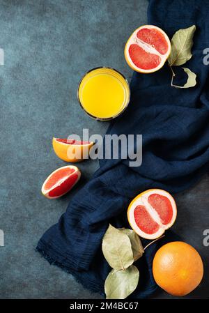 Saftige rote Grapefruit, ein Glas Saft und Scheiben auf blauem Hintergrund mit dunkler Serviette. Konzept gesunde Ernährung. Draufsicht und Kopierbereich. Stockfoto