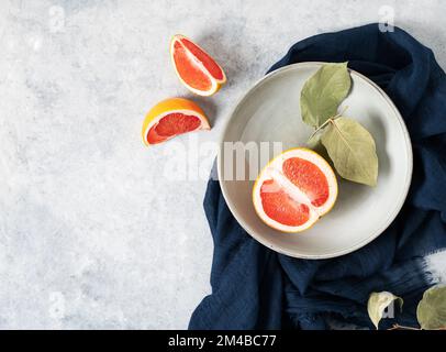 Saftige rote Grapefruit auf einem Teller und Scheiben auf blauem Hintergrund mit dunkler Serviette. Konzept gesunde Ernährung. Draufsicht und Kopierbereich. Stockfoto