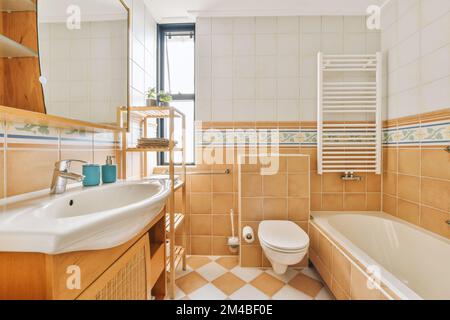 Badezimmer mit gefliesten Wänden und Holzschrank, Waschtisch, Badewanne, Toilette, Waschbecken und Badewanne Stockfoto