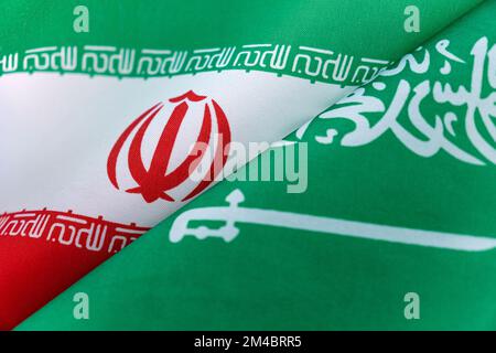 Die Flagge Saudi-Arabiens und des Irans, die mit Rissen gespalten sind, der Konflikt, die Beziehungen Saudi-Arabiens und des Irans, das Kriegskonzept Stockfoto