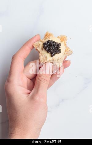 Schwarze Kaviar-Vorspeisen, Brotsterne mit Butter in einer menschlichen Hand auf weißem Hintergrund, Draufsicht Vertikal Stockfoto
