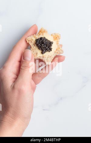 Schwarze Kaviar-Vorspeisen, Brotsterne mit Butter in einer menschlichen Hand auf weißem Hintergrund, Draufsicht Vertikal Stockfoto