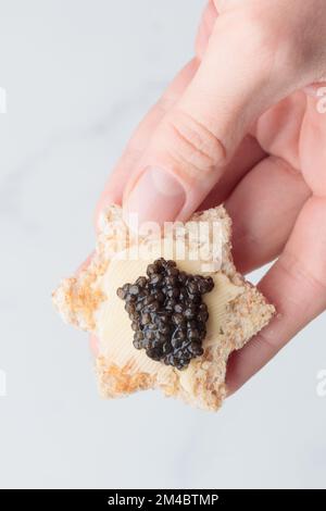 Schwarze Kaviar-Vorspeisen, Brotsterne mit Butter in einer menschlichen Hand auf weißem Hintergrund, Draufsicht Vertikal Stockfoto