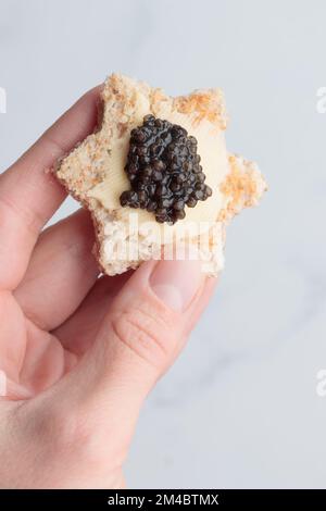 Schwarze Kaviar-Vorspeisen, Brotsterne mit Butter in einer menschlichen Hand auf weißem Hintergrund, Draufsicht Vertikal Stockfoto