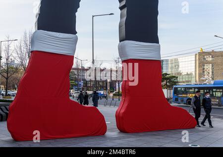 Seoul, Südkorea. 20.. Dezember 2022. Die Menschen gehen an der kinetischen Skulptur „Hammering man“ vorbei und tragen die roten Socken des Weihnachtsmanns vor dem Heungkuk Building. Die Skulptur, die am 4. Juni 2002 installiert wurde und Teil einer Serie ist, die von einem amerikanischen Bildhauer Jonathan Borofsky entworfen wurde, gilt als eines der Wahrzeichen von Seoul. Kredit: SOPA Images Limited/Alamy Live News Stockfoto