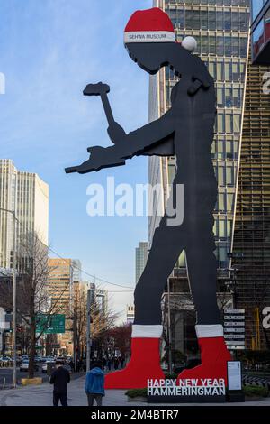 Seoul, Südkorea. 20.. Dezember 2022. Die Leute gehen vorbei an der kinetischen Skulptur „Hammering man“ mit dem roten Hut und den Socken des Weihnachtsmanns vor dem Heungkuk Building. Die Skulptur, die am 4. Juni 2002 installiert wurde und Teil einer Serie ist, die von einem amerikanischen Bildhauer Jonathan Borofsky entworfen wurde, gilt als eines der Wahrzeichen von Seoul. Kredit: SOPA Images Limited/Alamy Live News Stockfoto