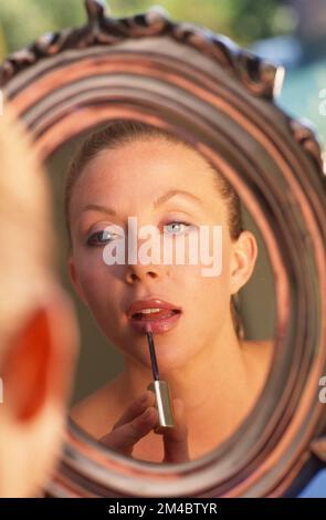 Junge Frau vor einem ovalen Spiegel, die Lipgloss aufträgt Stockfoto