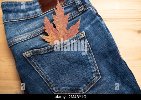 Ahornblatt in einer Jeanstasche, auf einem Holzregal. Saisonales Verkaufskonzept. Speicherplatz kopieren. - Flatley. - Was? Stockfoto