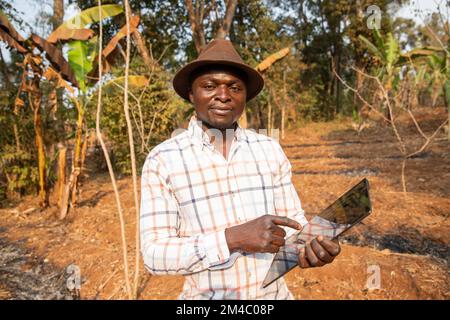 Ein afrikanischer Bauer auf seinem Feld mit einem Tablet in der Hand, Technologie in der Landwirtschaft in Afrika Stockfoto