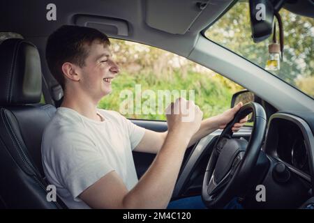 Der fröhliche junge Fahrer vor dem Lenkrad hält die Faust fest und feiert den Erfolg Stockfoto