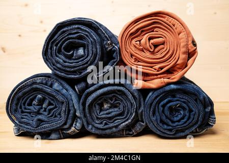 Die Jeans sind aufgerollt und gestapelt auf einem Holzhintergrund. Stockfoto