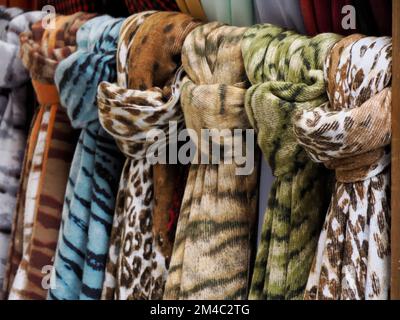 Farbenfrohe Schals im Vintage-Stil mit verschiedenen Mustern, Farben und Texturen, die an einem Regal in einem Outdoor-Shop hängen Stockfoto