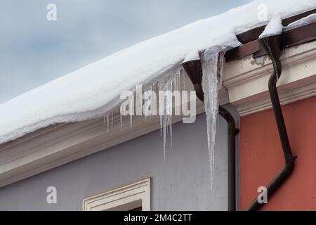 Eiszapfen hängen an einem kalten Winter- oder Frühlingstag vom Dach eines Gebäudes in der Stadt Stockfoto