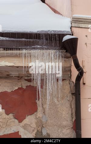 Eiszapfen hängen an einem kalten Winter- oder Frühlingstag von einem Dach eines Gebäudes in der Stadt Stockfoto