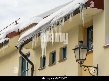 Eiszapfen hängen an einem kalten Winter- oder Frühlingstag vom Dach eines Gebäudes in der Stadt Stockfoto
