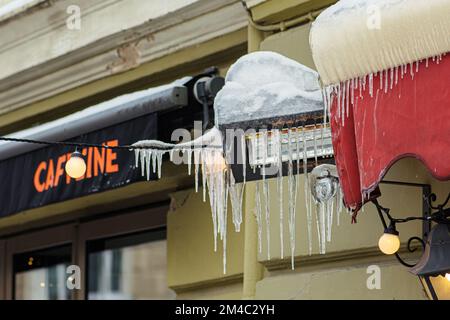 Eiszapfen, die an einer Straßenlaterne hängen, und elektrische Kabel in der Nähe eines Restaurants oder Cafés in der Stadt an einem kalten Winter- oder Frühlingstag in Vilnius, Litauen Stockfoto