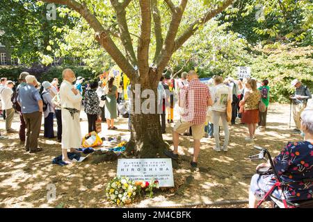 Die Menschen versammeln sich in der Nähe des Kirschbaums, der zum Gedenken an die Opfer von Hiroshima während einer Gedenkveranstaltung im Zentrum von London gepflanzt wurde. Stockfoto