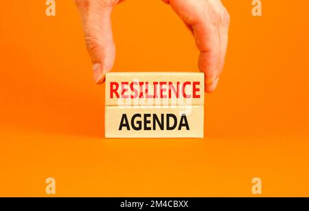 Symbol für Resilienz-Agenda. Konzeptwort „Resilience Agenda“ auf Holzblöcken getippt. Schöner orangefarbener Tischhintergrund. Geschäftsmannshand. Geschäftlich Stockfoto