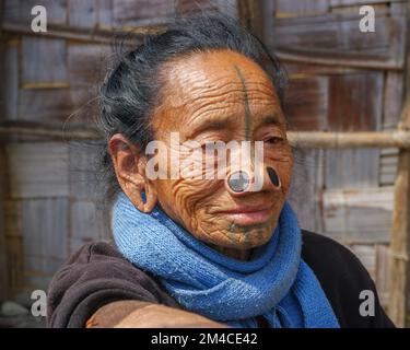 Ziro, Arunachal Pradesh, Indien - 03 04 2014 : Porträt der alten Apatani-Stammesfrau mit traditionellen Gesichts-Tattoos und Nasenstöpseln mit blauem Schal Stockfoto