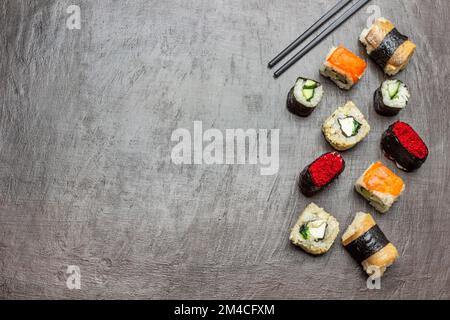 Sushi verschiedener Art. Speicherplatz kopieren. Flach verlegt. Schwarze Essstäbchen. Brauner Hintergrund. Stockfoto
