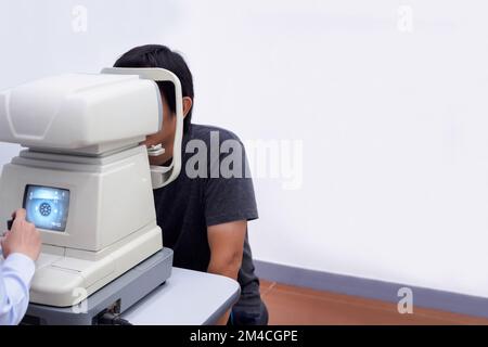 Junger, gutaussehender Asiate macht eine Augenuntersuchung mit einem optischen Augen-Testgerät Stockfoto