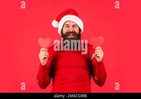 Kalte Tage. Warme Herzen. Willkommen Weihnachten in deinem Herzen. Ein hübscher Mann liebt Winterferien, roter Hintergrund. Der Kerl trägt einen Weihnachtsmann-Hut. Frohe weihnachten und Stockfoto