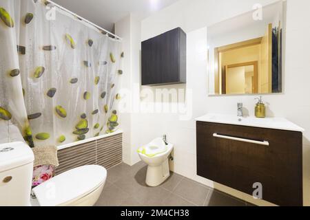 Badezimmer mit dunklem Wandschrank aus Holz mit großer Schublade, rahmenlosem quadratischem Spiegel und Duschablage mit Duschvorhang Stockfoto