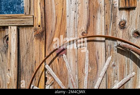 Ein kaputtes Wagenrad neigt sich an die Wand einer rustikalen Holzhütte Stockfoto