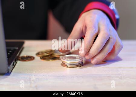 Berechnung eines Münzstapels auf einem Tisch neben einem Laptop durch eine Person auf farbigem Hintergrund Stockfoto