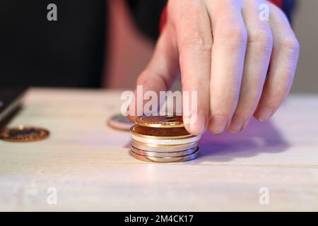 Berechnung eines Münzstapels auf einem Tisch neben einem Laptop durch eine Person auf farbigem Hintergrund Stockfoto