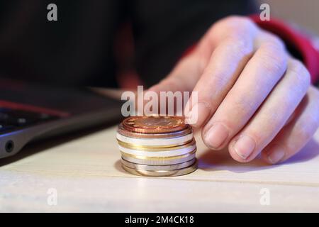 Berechnung eines Münzstapels auf einem Tisch neben einem Laptop durch eine Person auf farbigem Hintergrund Stockfoto