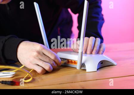 Person, die das Internetkabel des Routers auf dem Tisch mit farbigem Hintergrund einsteckt Stockfoto