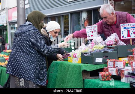 Gemüsehändler auf dem Walthamstow Market, London, Großbritannien, dem längsten Markt für Außenbereiche in Europa, mit Händlern und Händlern, die Käufer bedienen, mit Preisen in Pfund Sterling Stockfoto