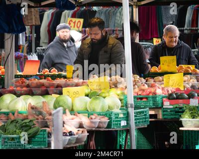 Gemüsehändler auf dem Walthamstow Market, London, Großbritannien, dem längsten Markt für Außenbereiche in Europa, mit Händlern und Händlern, die Käufer bedienen, mit Preisen in Pfund Sterling Stockfoto