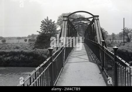 1950er, historisch, Ford Bridge, Northenden Ford, Didsbury, Manchester, England, Großbritannien. Die Überquerung ist weithin als Simon Bridge bekannt, da ihr Bau von einem Einheimischen Henry Simon finanziert wurde. Die eiserne Fußgängerbrücke über den Fluss Mersey wurde 1901 an der Stelle eines alten ford gebaut, um den Zugang zu einem Gebiet zu verbessern, das als Poor's Field bekannt ist, da dieses Land der örtlichen Kirche Miete brachte. Historisch gesehen war der ford ein Tor in die Stadt Manchester und zurück. Stockfoto