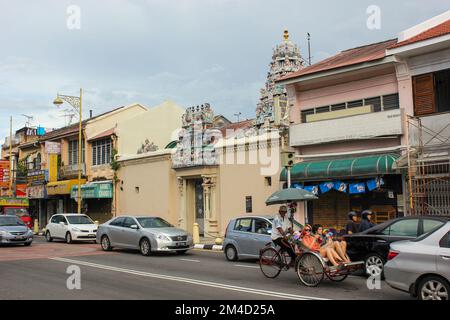 Georgetown, Penang, Malaysia - November 2012: Eine Straßenszene mit einem alten hinduistischen Tempel, Oldtimer-Shops und einem Mann in einer Rikscha mit Touristen Stockfoto